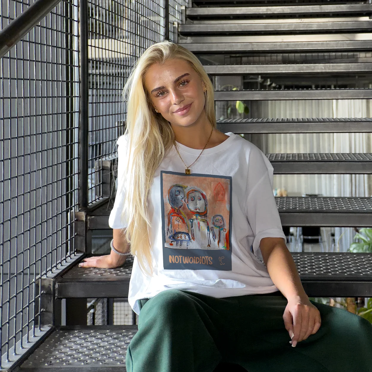 Model wearing a white t-shirt with a framed illustration print, industrial staircase behind