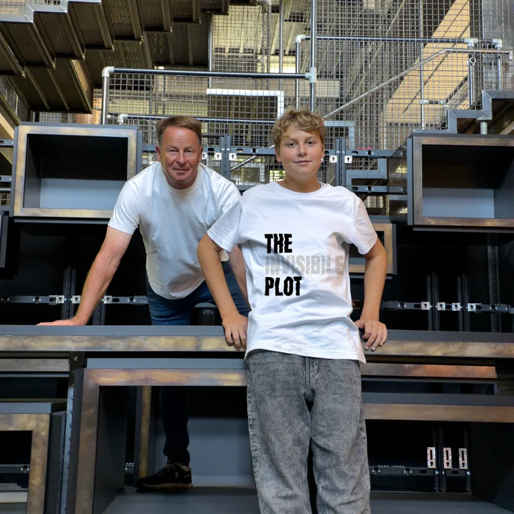 Accomplices wearing t-shirts with artist designs from The Invisible Plot — two accomplices in an industrial space