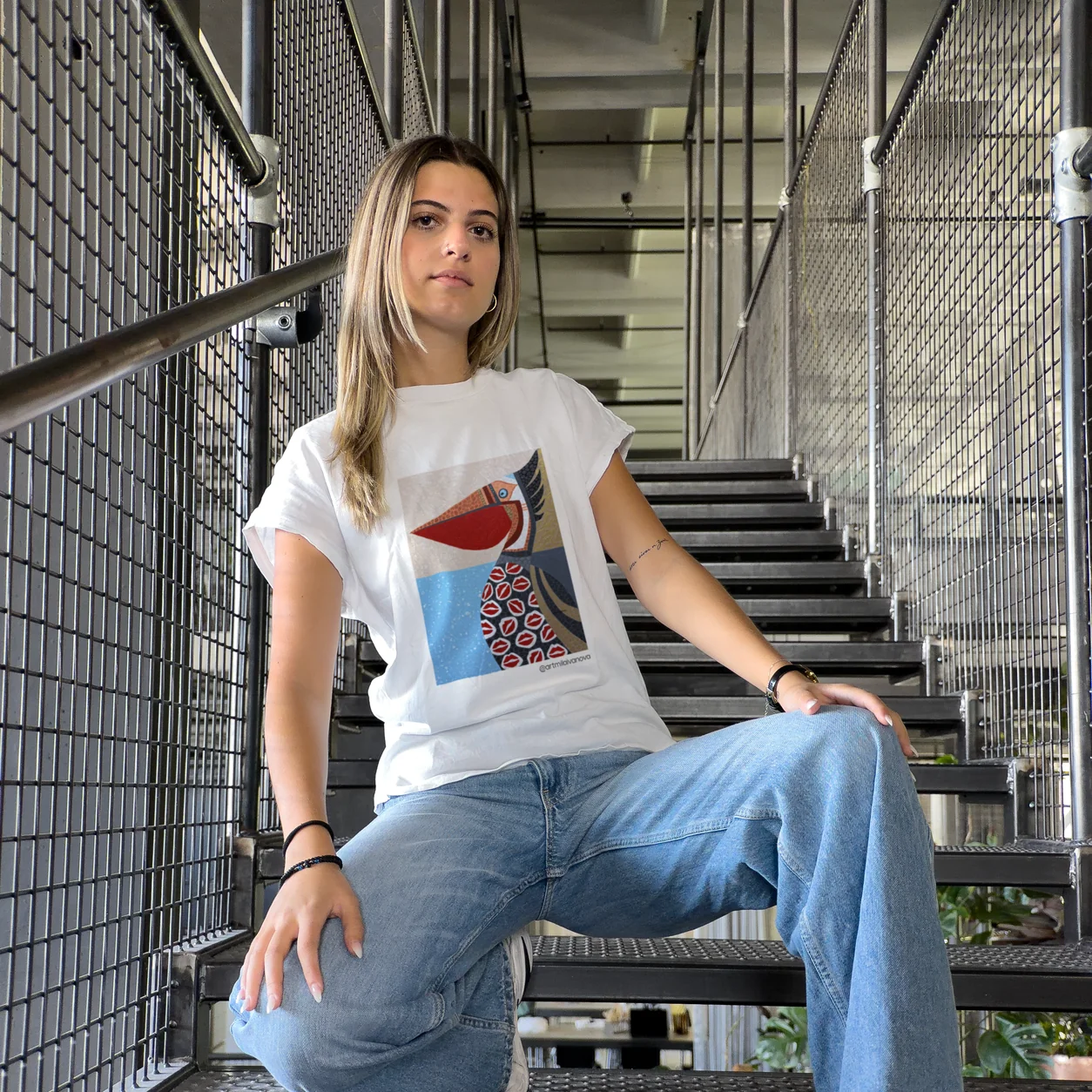 Model seated on an industrial staircase wearing a t-shirt with a red and blue artwork print