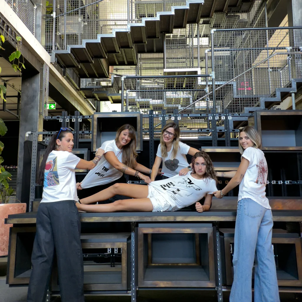 Accomplices wearing t-shirts with artist designs from The Invisible Plot — group posing on a metal table